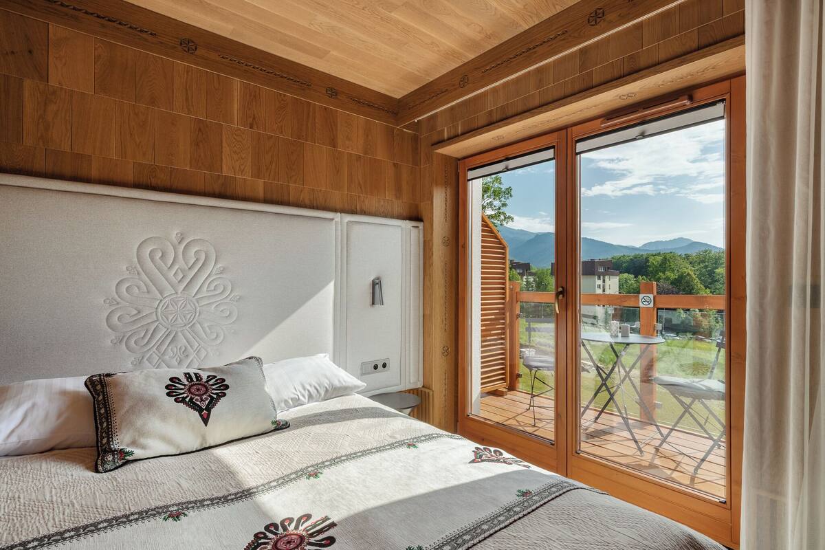 Une chambre dotée d’un grand lit, d’une tête de lit décorative et offrant une vue sur une terrasse et les montagnes, grâce à une porte-fenêtre coulissante.