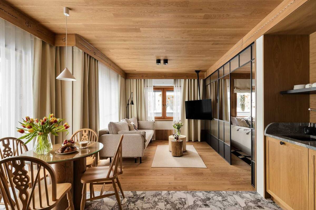 Un intérieur moderne avec un plafond en bois, un coin repas comprenant une table ronde et des chaises, un canapé, un téléviseur et un espace cuisine.