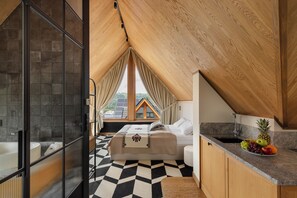 Ein Schlafzimmer mit schrägen Wänden, einem Bett, einem Nachttisch, einem Waschbecken und einer Obstschale auf der Arbeitsfläche.