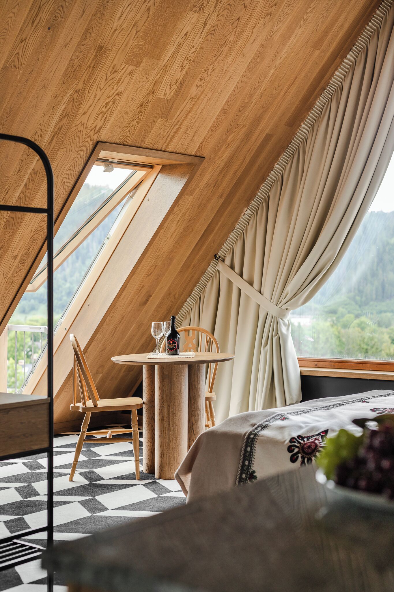 A cozy room with a sloped ceiling, a dining table with chairs, a bed, and a window with curtains.