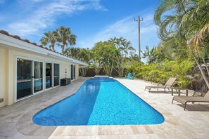 Une piscine rectangulaire, bordée d’une terrasse carrelée et entourée de palmiers et de chaises longues.