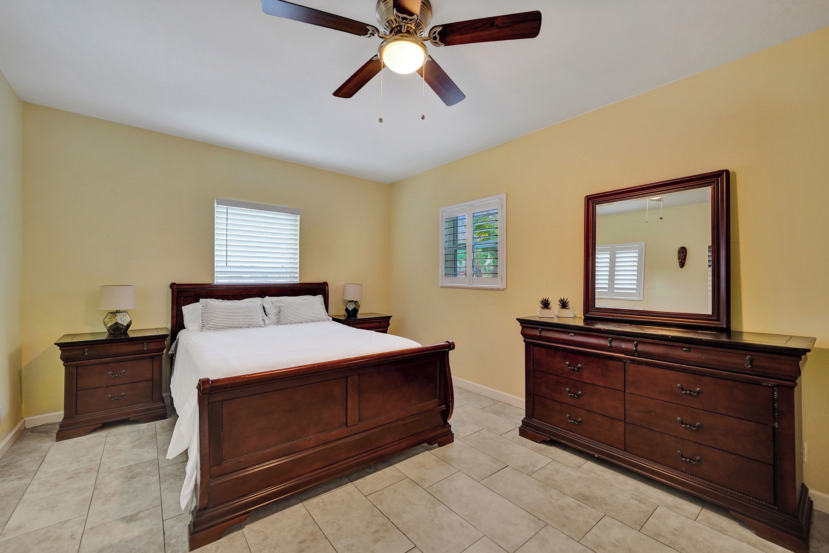 A bedroom with a wooden bed, nightstands, a dresser, a ceiling fan, and a large mirror.