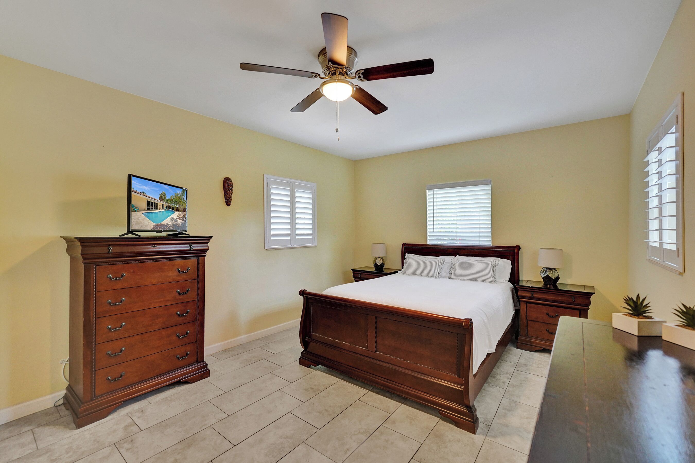 A bedroom with a bed, dresser, nightstands, a ceiling fan, and a picture on the wall.