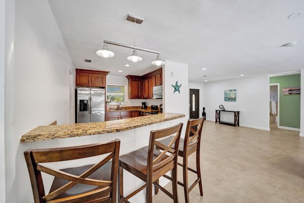 A modern kitchen with granite countertops, wooden chairs, and stainless steel appliances.