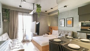 A modern hotel room with a bed, a sofa, a dining table set for two, and a kitchen area.