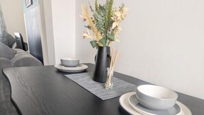 A modern dining area with a black table, white plates, and a vase with dried flowers. - Charming Newcastle Home With Garden, Perfect for Families & Contractors (Jarrow)