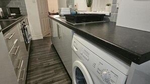 A modern kitchen with a built-in washer and dryer, stainless steel appliances, and a dark wood floor. - Charming Newcastle Home With Garden, Perfect for Families & Contractors (Jarrow)