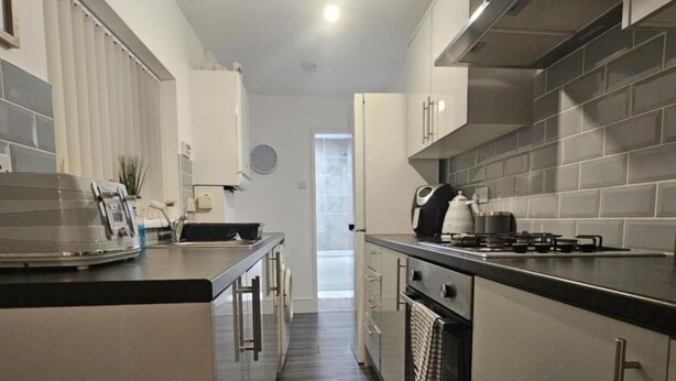 A modern kitchen with grey cabinetry, a central island, and a view into the adjacent living area. - Charming Newcastle Home With Garden, Perfect for Families & Contractors (Jarrow)