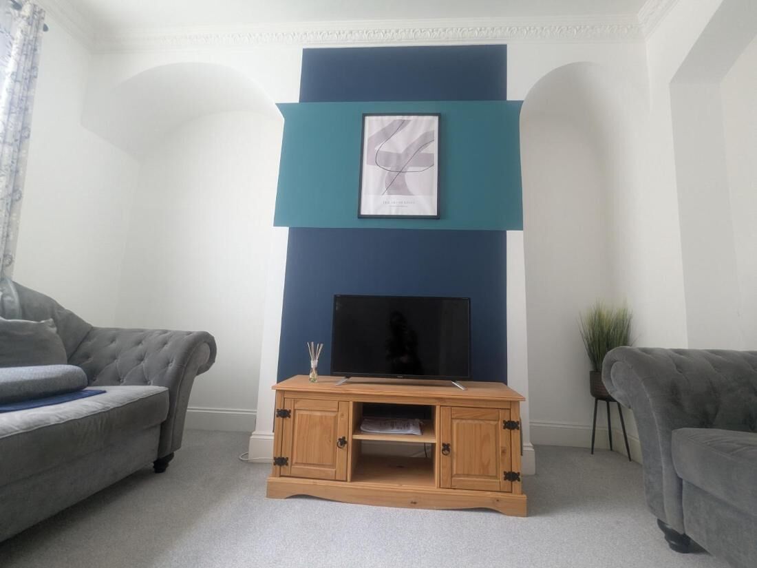 A living room with a blue accent wall, a framed artwork above a flat-screen TV, and a wooden entertainment unit.