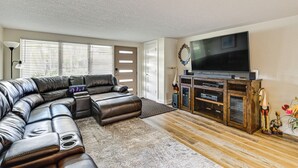Een moderne woonkamer met een hoekbank, een flatscreen televisie, houten vloeren en een decoratief vogelsulptuur.