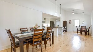 Un vaste espace dédié à la salle à manger, avec une table et des chaises en bois, une cuisine en arrière-plan et un plafond haut orné de luminaires suspendus.