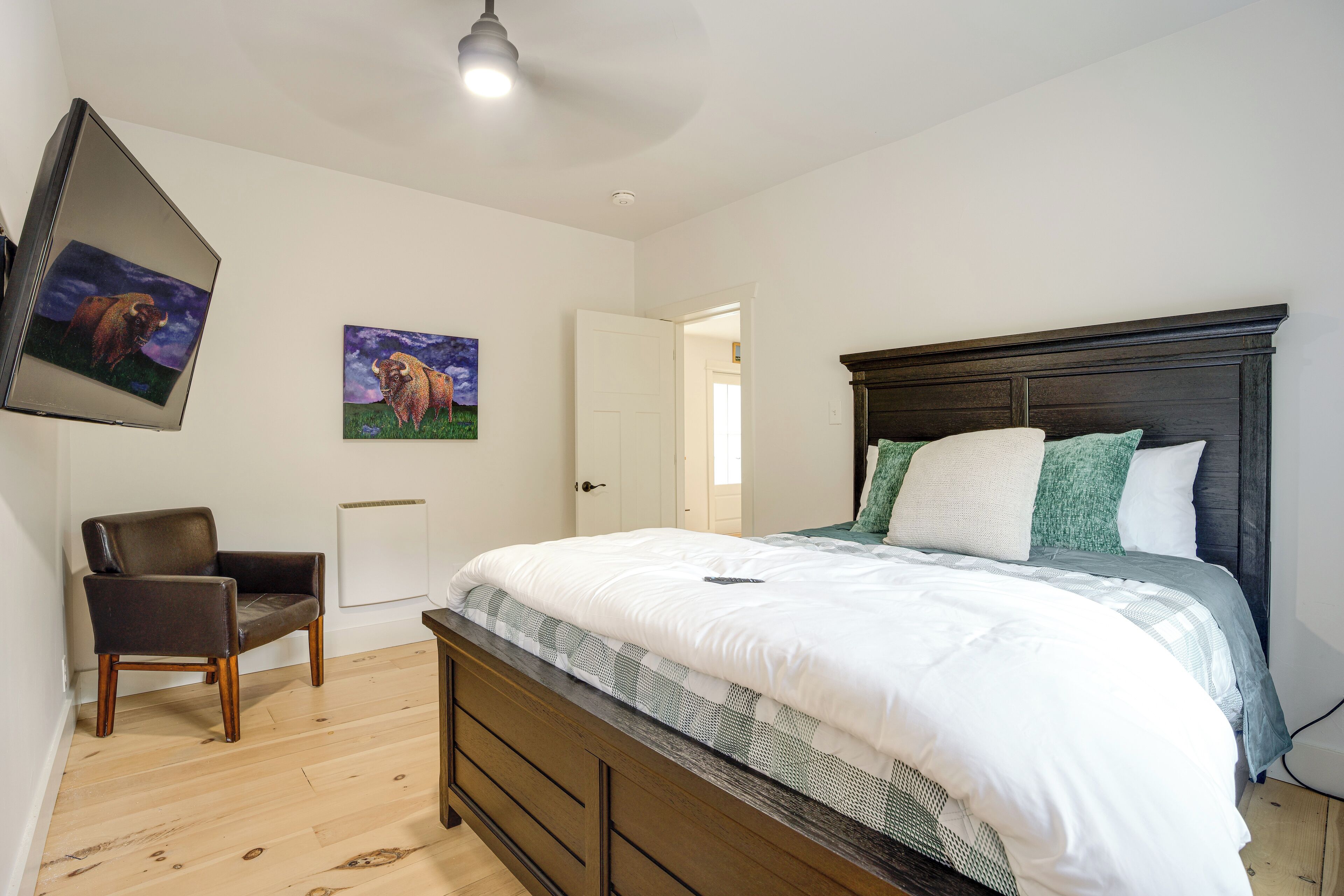 A bedroom with a wooden bed, a chair, and two paintings on the wall.