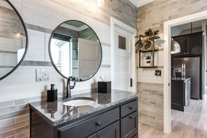 Un baño moderno con encimera de granito, dos espejos redondos, un lavamanos blanco y un mueble de tocador negro.