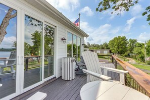 Una terraza con sillas Adirondack blancas, una mesa de madera y vistas a un lago y árboles.