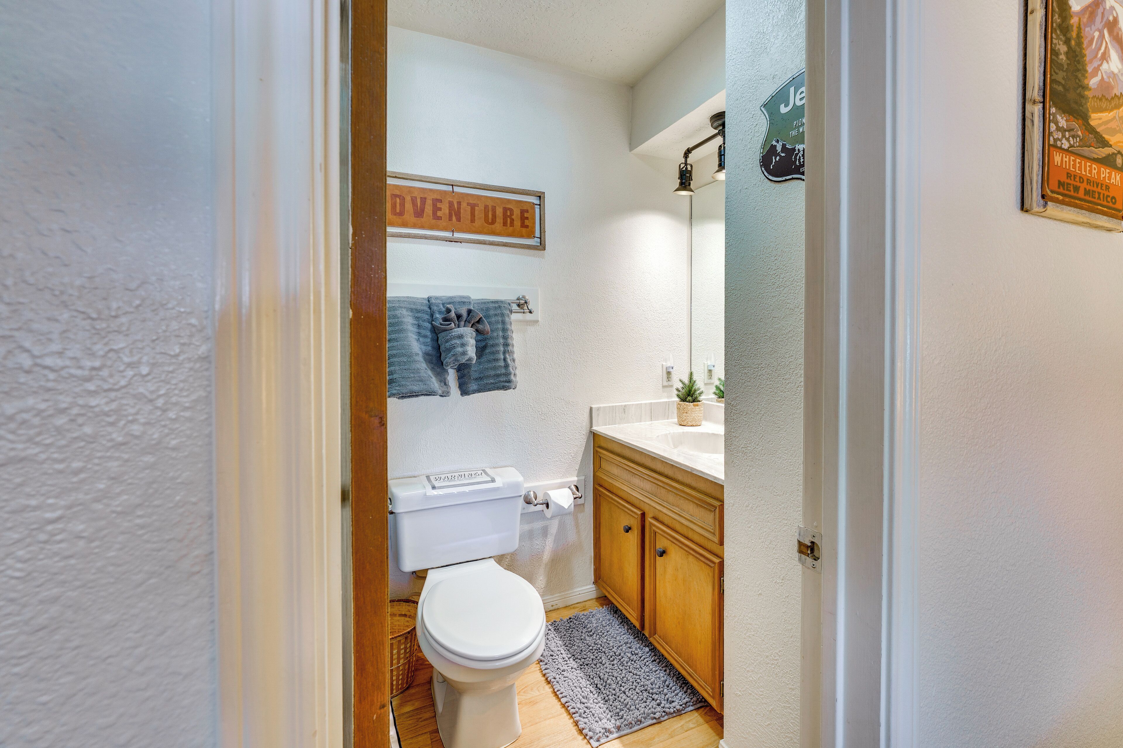 A compact bathroom with a toilet, wooden cabinets, a sink, and a towel rack with towels.