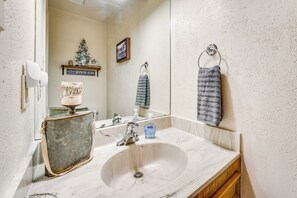 A bathroom with a marble sink, a mirror, a towel rack, and a shelf with decorative items. - Hike, Bike & Ski: Red River Condo w/ Spa Access (Red River)