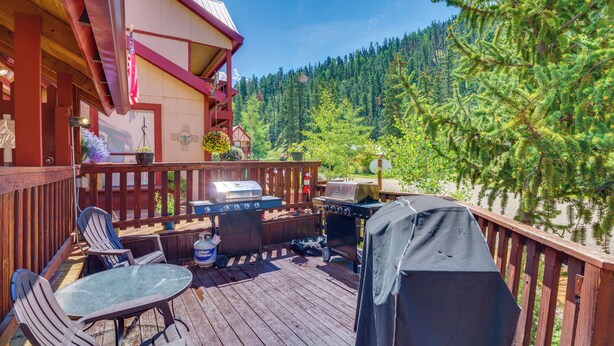 Une terrasse en bois, dotée de mobilier d’extérieur, de barbecues et offrant une vue sur une montagne boisée.