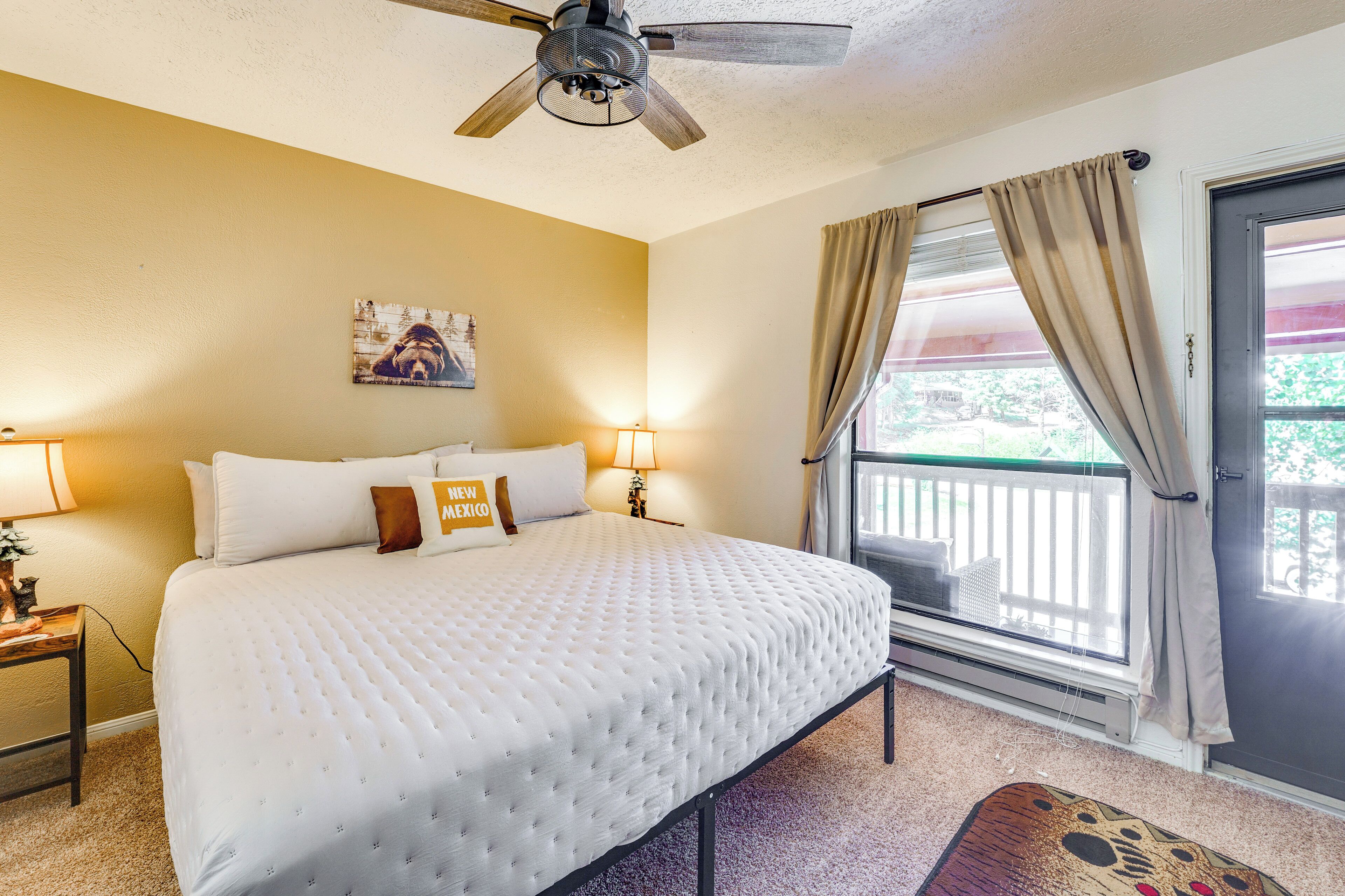 Une chambre d’hôtel avec un lit, deux lampes de chevet, un ventilateur de plafond, une fenêtre avec des rideaux et un petit tapis.