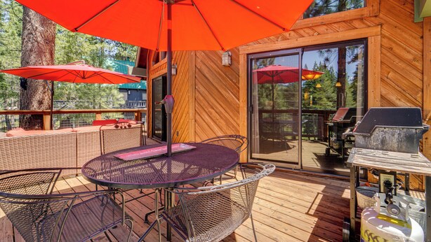 A wooden deck with a round table and chairs, red umbrellas, and a grill. - Live Like a Local in Truckee: Luxe Cabin Near Dtwn (Truckee)