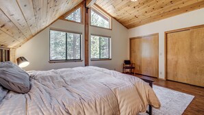 A bedroom with a large bed, wooden ceiling beams, and multiple windows. - Live Like a Local in Truckee: Luxe Cabin Near Dtwn (Truckee)
