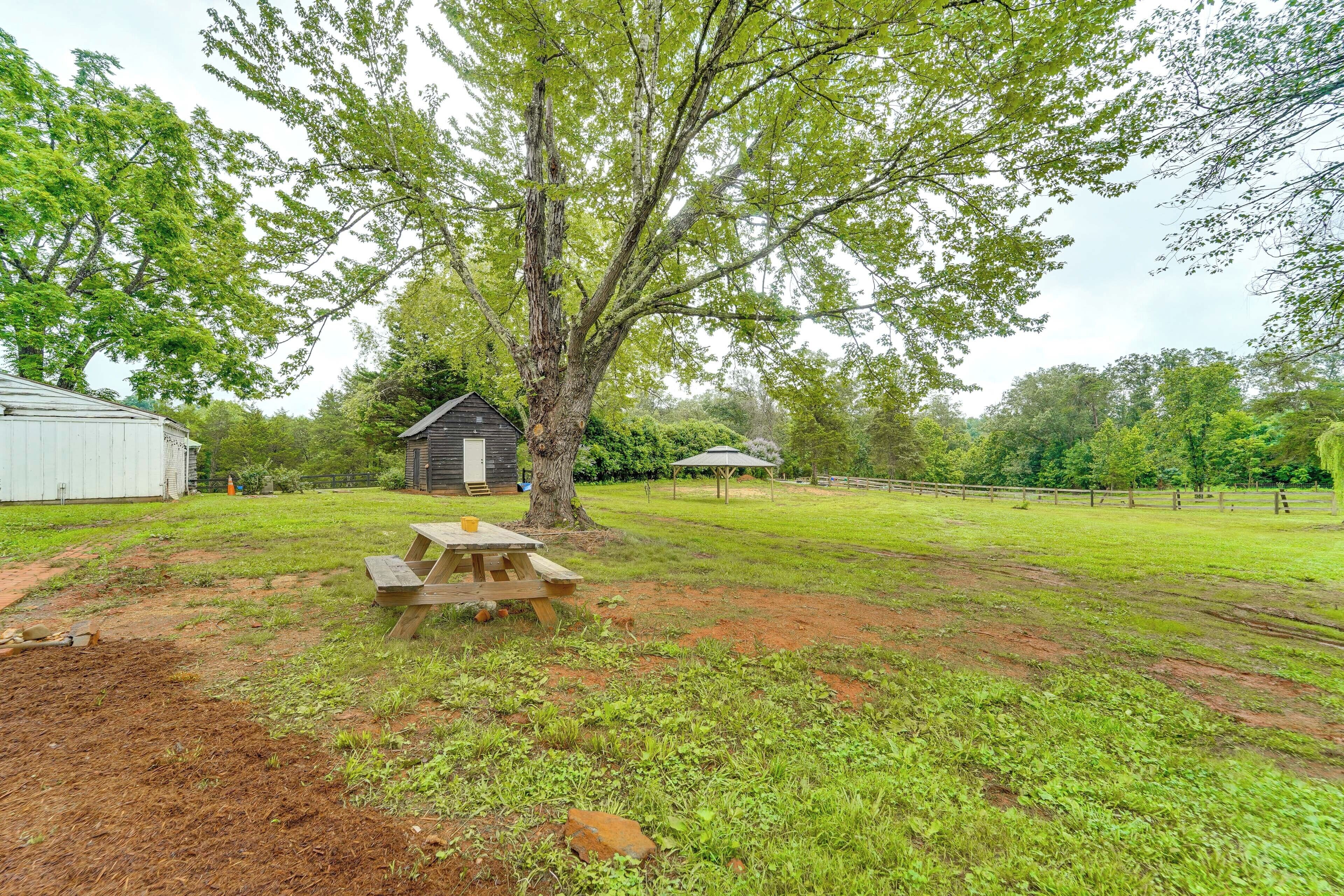 A picnic table in a grassy area with a tree and a small wooden structure in the background.