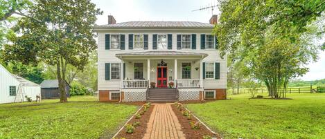 A two-story house with a red door, a front porch, and a brick pathway leading to the entrance.