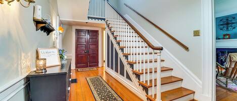 A wooden staircase with a white handrail, a dark wooden bench, and a welcome sign on the wall.