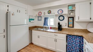 Una cocina con armarios blancos, un refrigerador de acero inoxidable, una encimera de granito, una cafetera y platos decorativos en la pared.