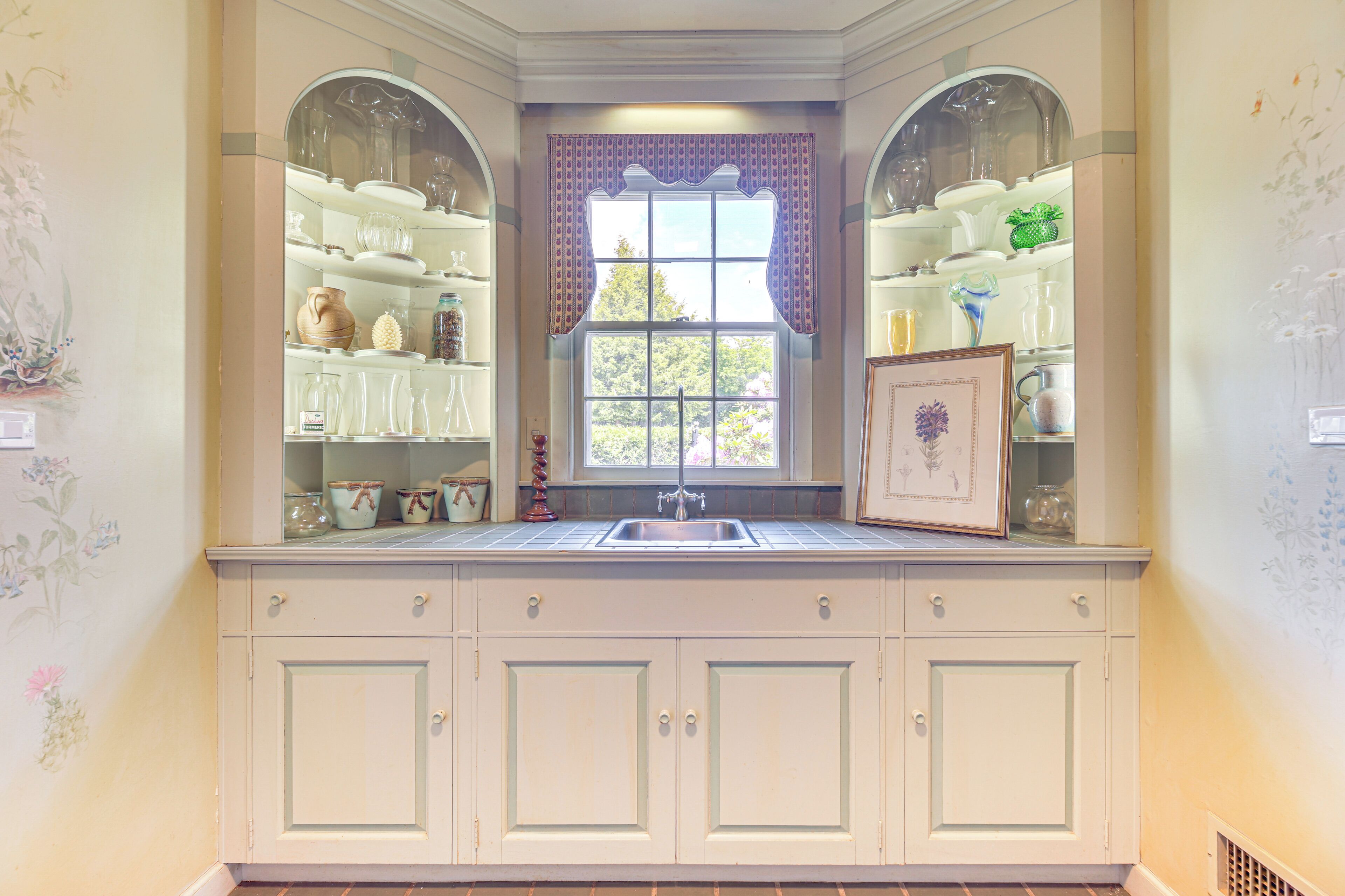 A kitchen with a window, cabinets, and shelves with dishes.