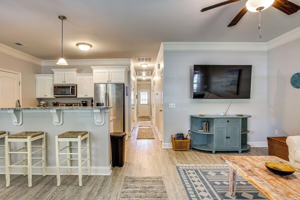 A modern kitchen with white cabinetry, a central island with stools, a microwave, and a refrigerator.