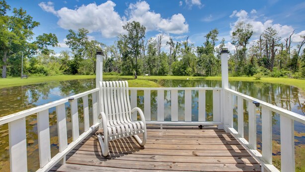 A wooden deck with a white railing, a single white chair, and a view of a pond and trees. - 'aunt Lucille's Place' - Cozy Cottage in Glenwood! (Glenwood)