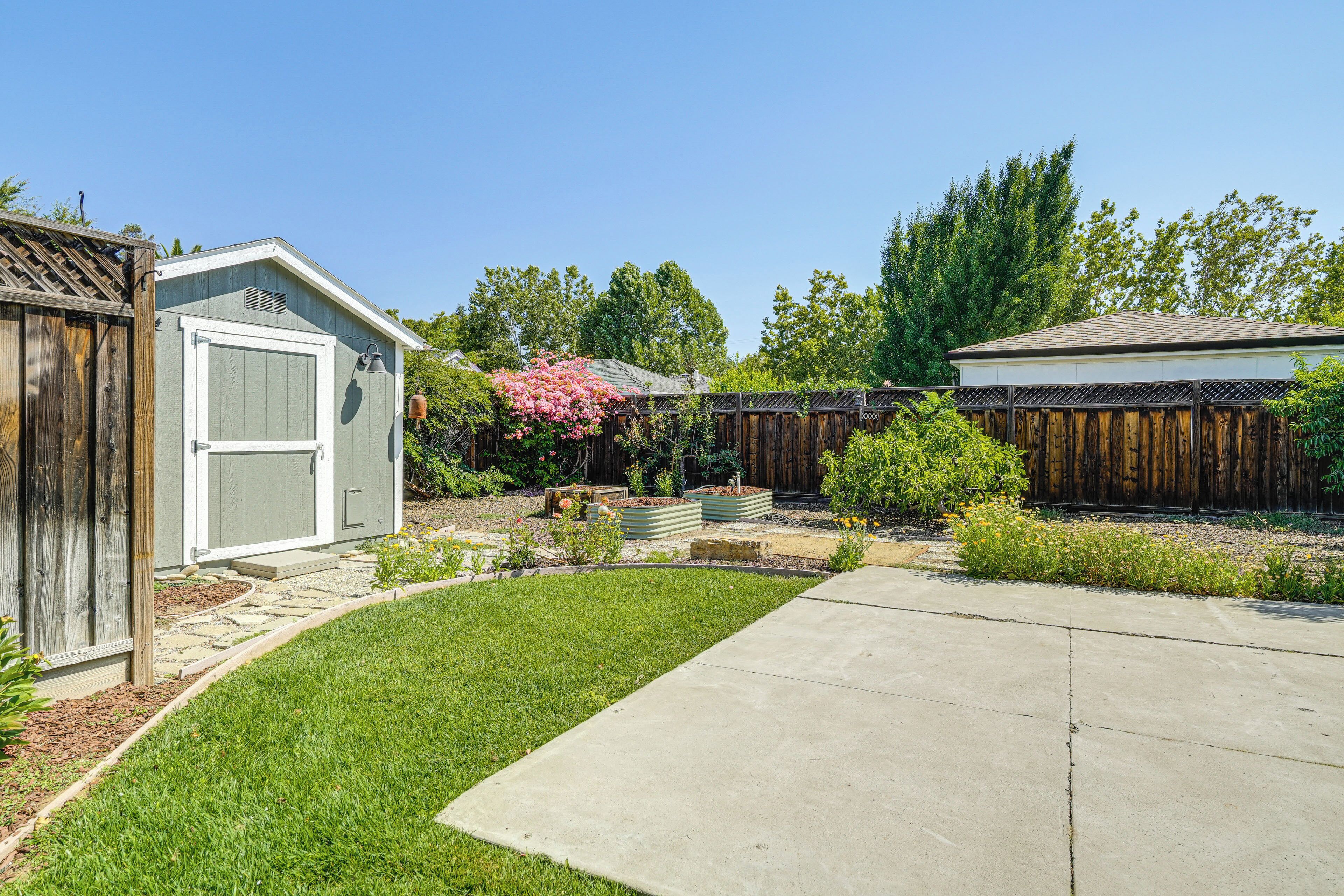 A backyard with a wooden fence, a shed, and a garden with various plants and flowers.