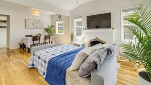 Quarto com cama, sofá cinza, ventoinha no teto, lareira, televisão e área de jantar com mesa e cadeiras.