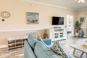 A living room with a blue sofa, a flat-screen TV, a wooden bench, and a painting on the wall.