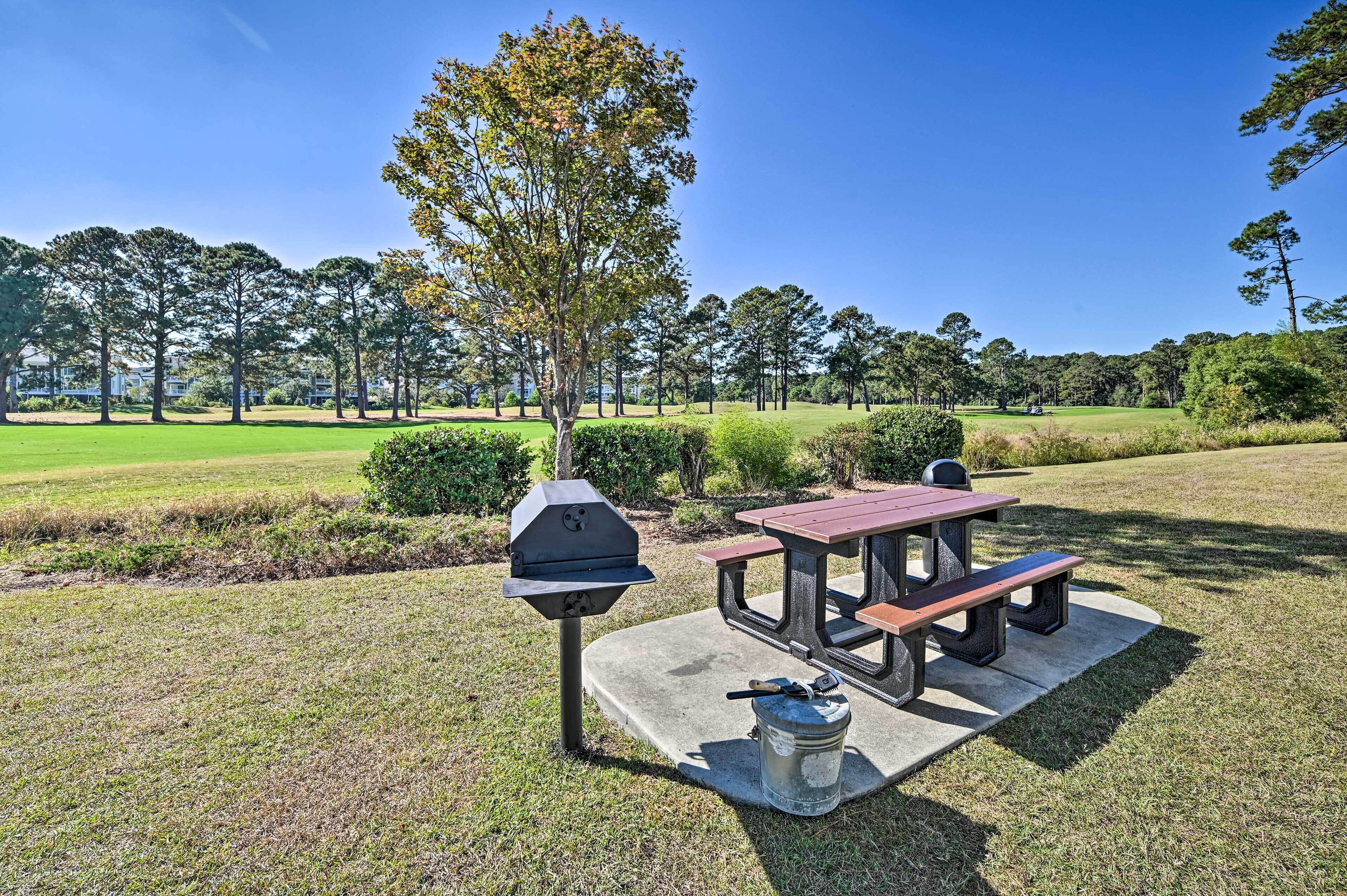 Een picknickplaats met een barbecue, tafel en bank, omgeven door gras en bomen.