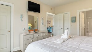 A bedroom with a large bed, a dresser, a TV mounted on the wall, and a bathroom visible through an open door. - Golf Course Getaway w/ Pool Access in Myrtle Beach (Myrtle Beach)