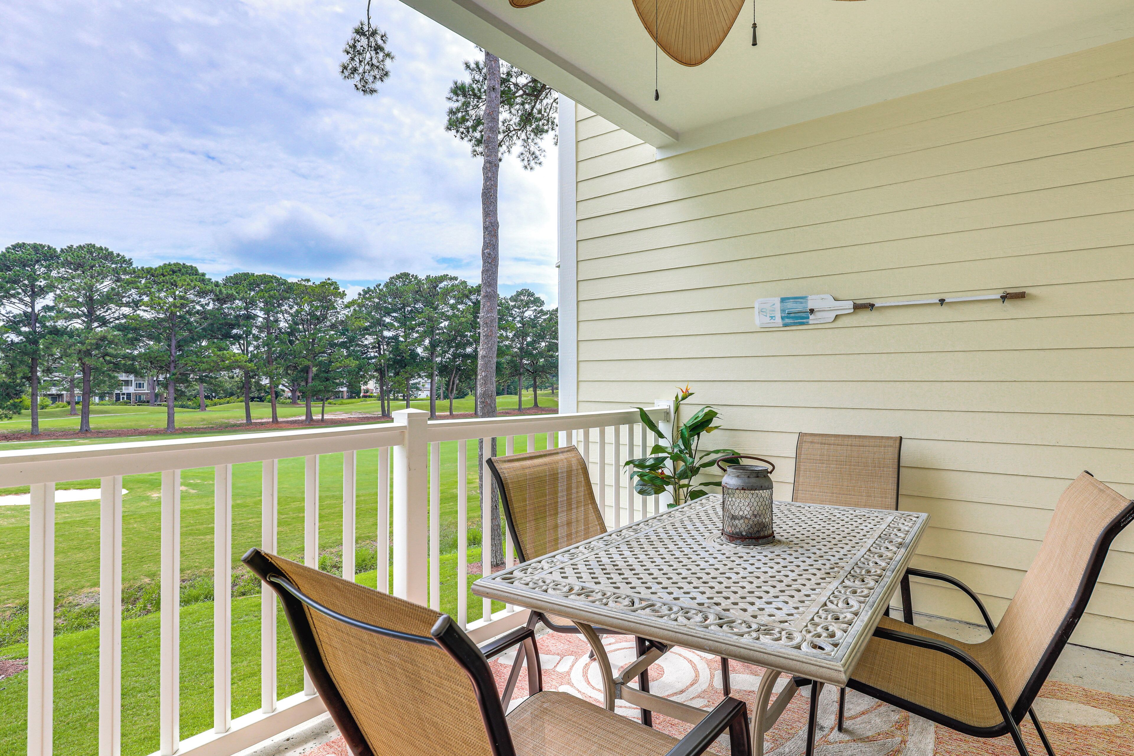 A covered patio with a table and chairs, a hanging light fixture, and a view of a green landscape.