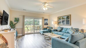 A spacious living room with a large sofa, a coffee table, and a ceiling fan. There is a sliding glass door leading to an outdoor patio area. - Golf Course Getaway w/ Pool Access in Myrtle Beach (Myrtle Beach)