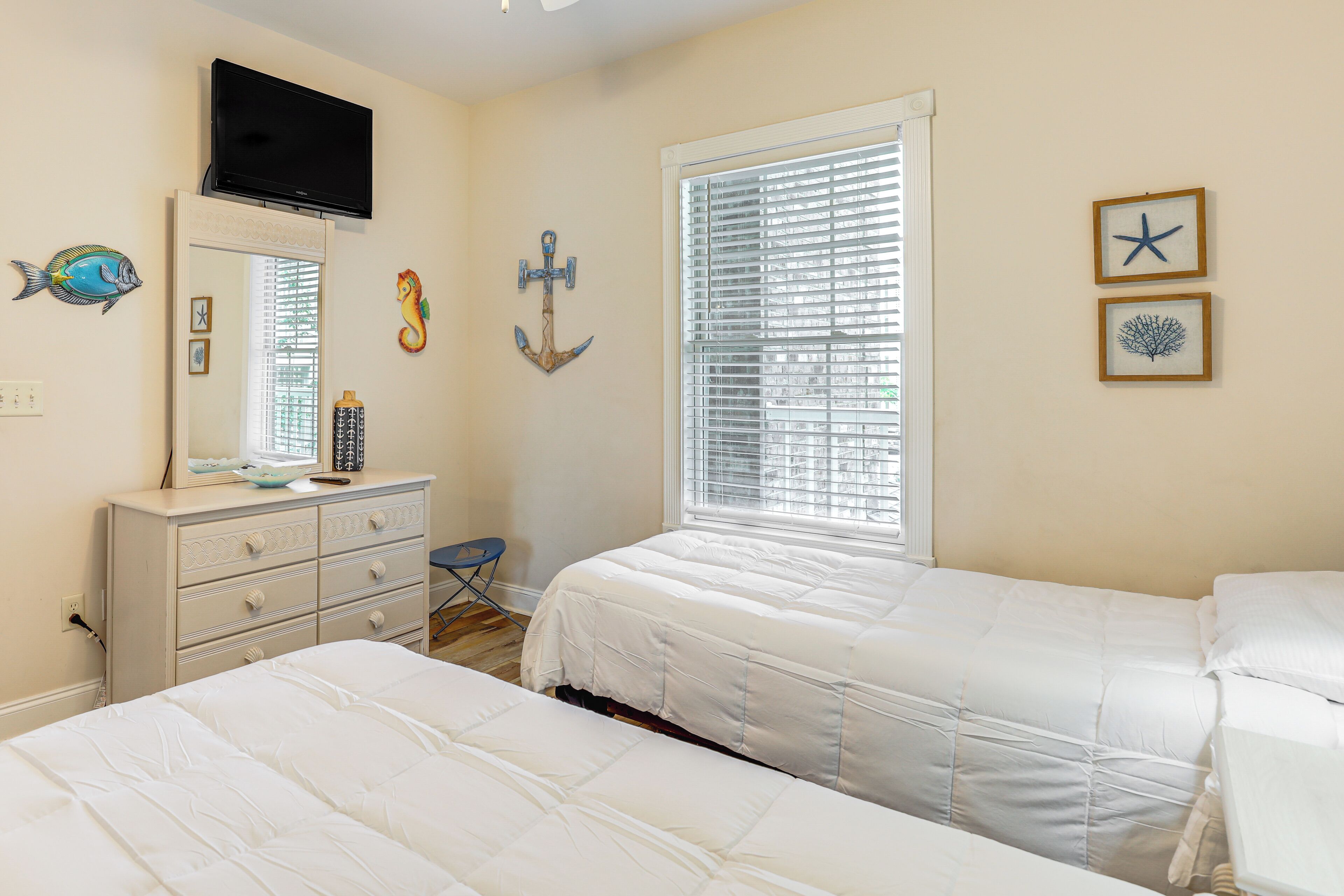 Een slaapkamer met twee bedden, een dressoir, een televisie en decoratie met nautische motieven.