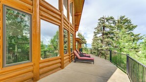 A wooden log cabin with large windows, a concrete deck, and a view of trees.