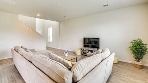A modern living room with a beige sectional sofa, a coffee table, a flat-screen TV, and a potted plant. - 4 Mi to Bear Creek Pioneers Park: NW Houston Home (Houston)