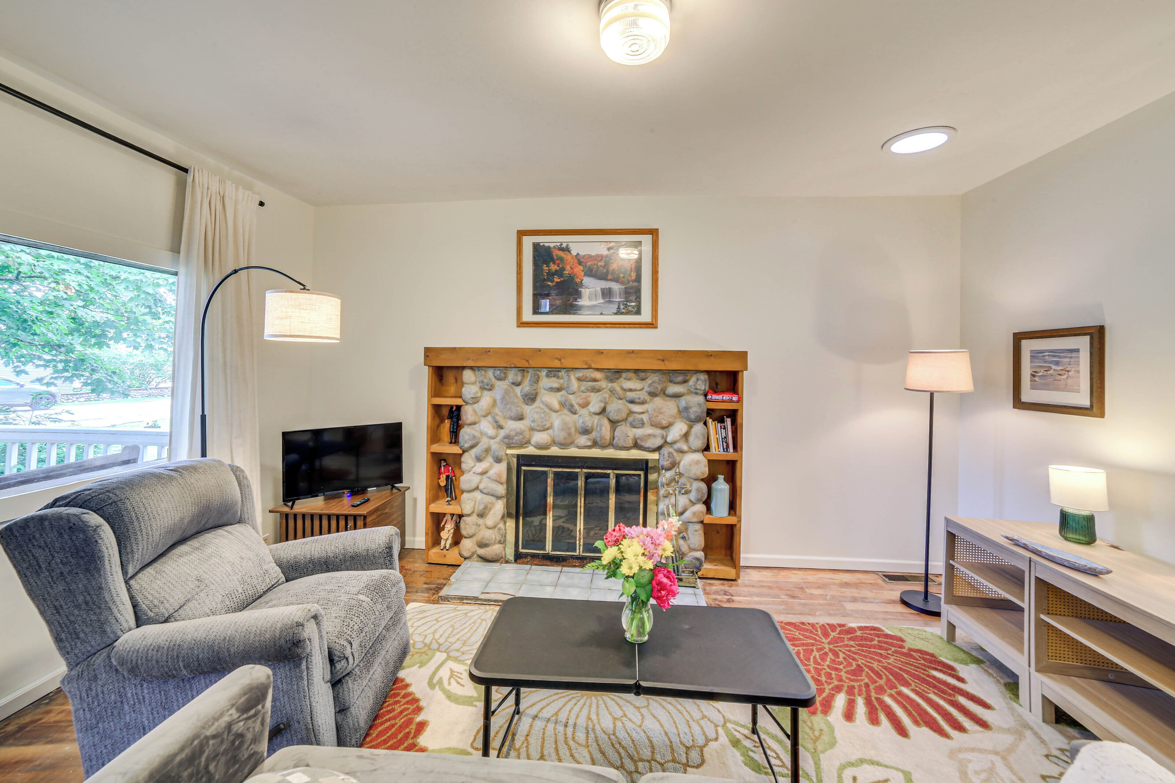 A living room with a stone fireplace, a television, a sofa, and a coffee table with flowers.