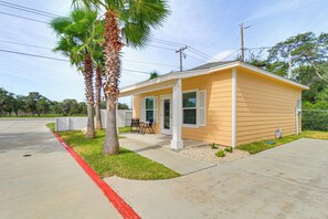 A single-story yellow building with a covered porch, palm trees, and a clear sky.