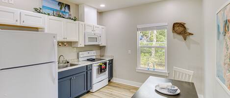 A kitchen with white cabinets, a microwave, and a stove. There is a window with a view of greenery outside.