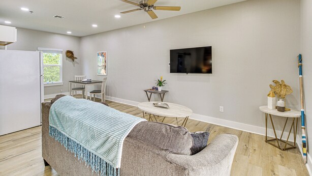 A modern living room with a sofa, a dining table, a TV, and a ceiling fan. - Fish & Swim On-site: Resort Retreat in Rockport! (Rockport)