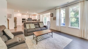 A spacious living room with a brown leather sofa, a wooden coffee table, and a large window with white curtains.