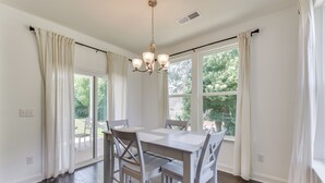 A dining area with a table and chairs, large windows, and a chandelier.