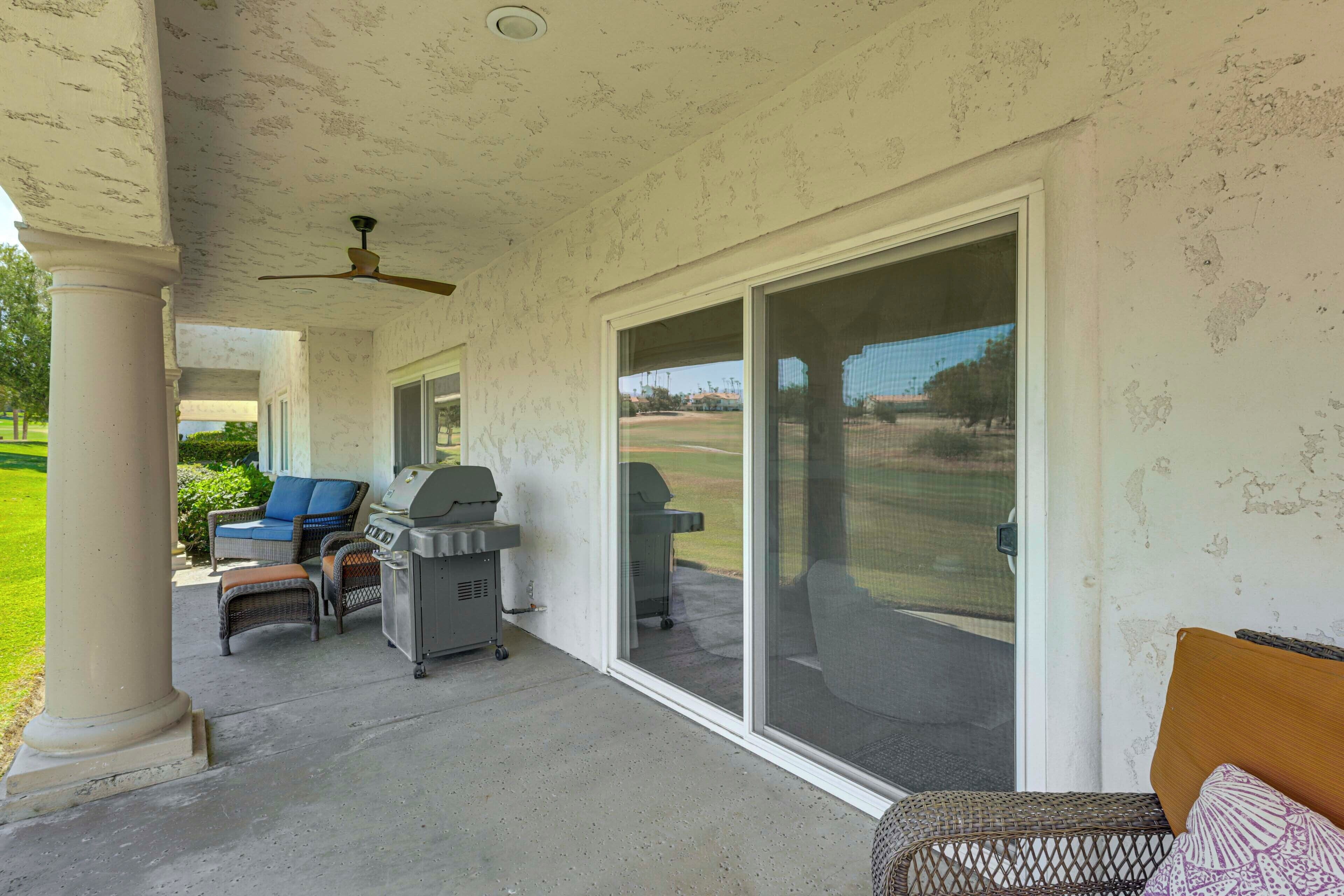 Un patio cubierto con una parrilla, asientos y vistas a un campo de golf.