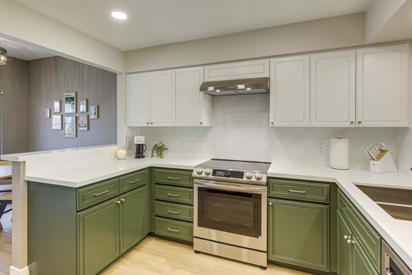 A modern kitchen with green cabinets, a stainless steel oven, and white countertops.