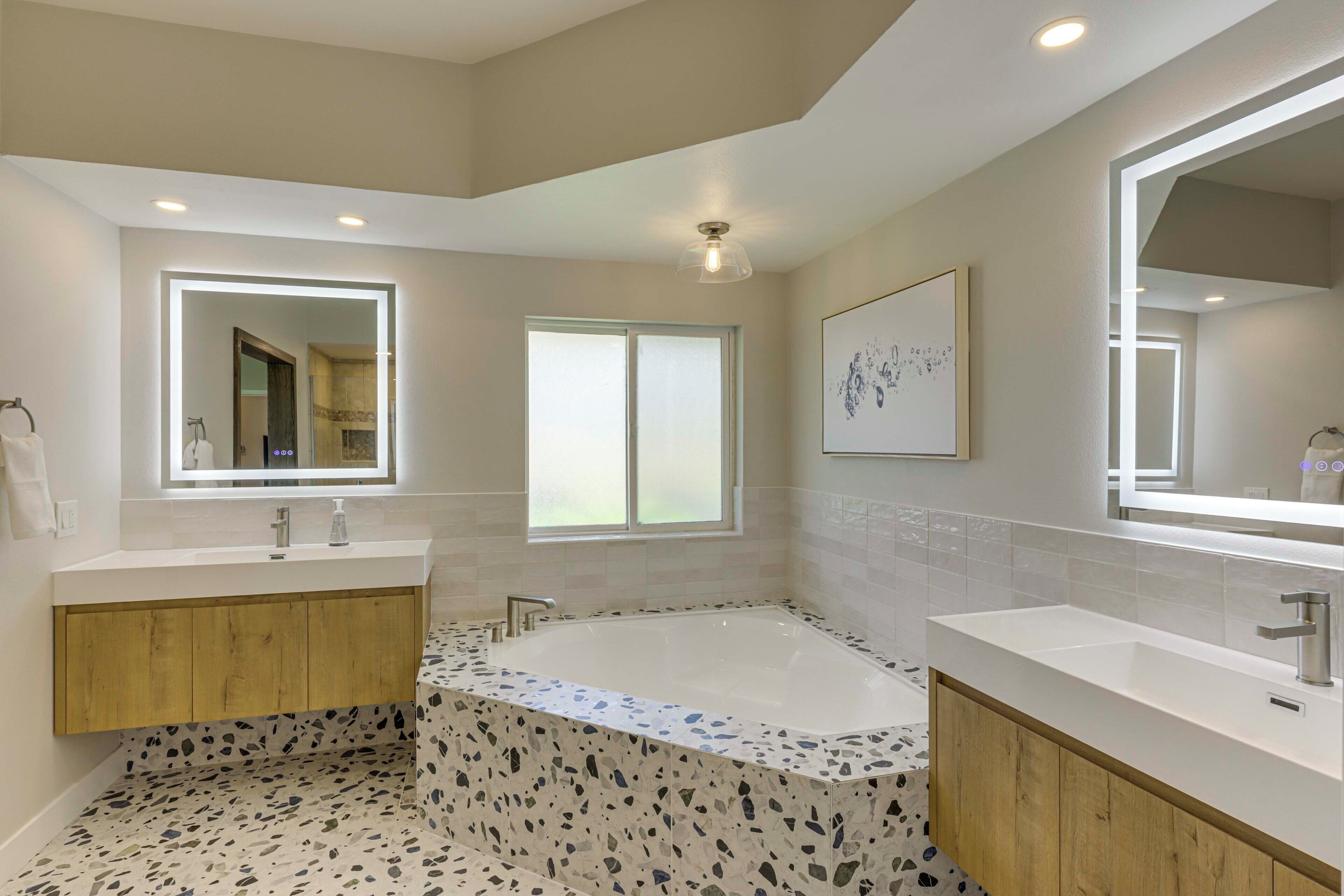 A modern bathroom with two sinks, a freestanding bathtub, and a large mirror.